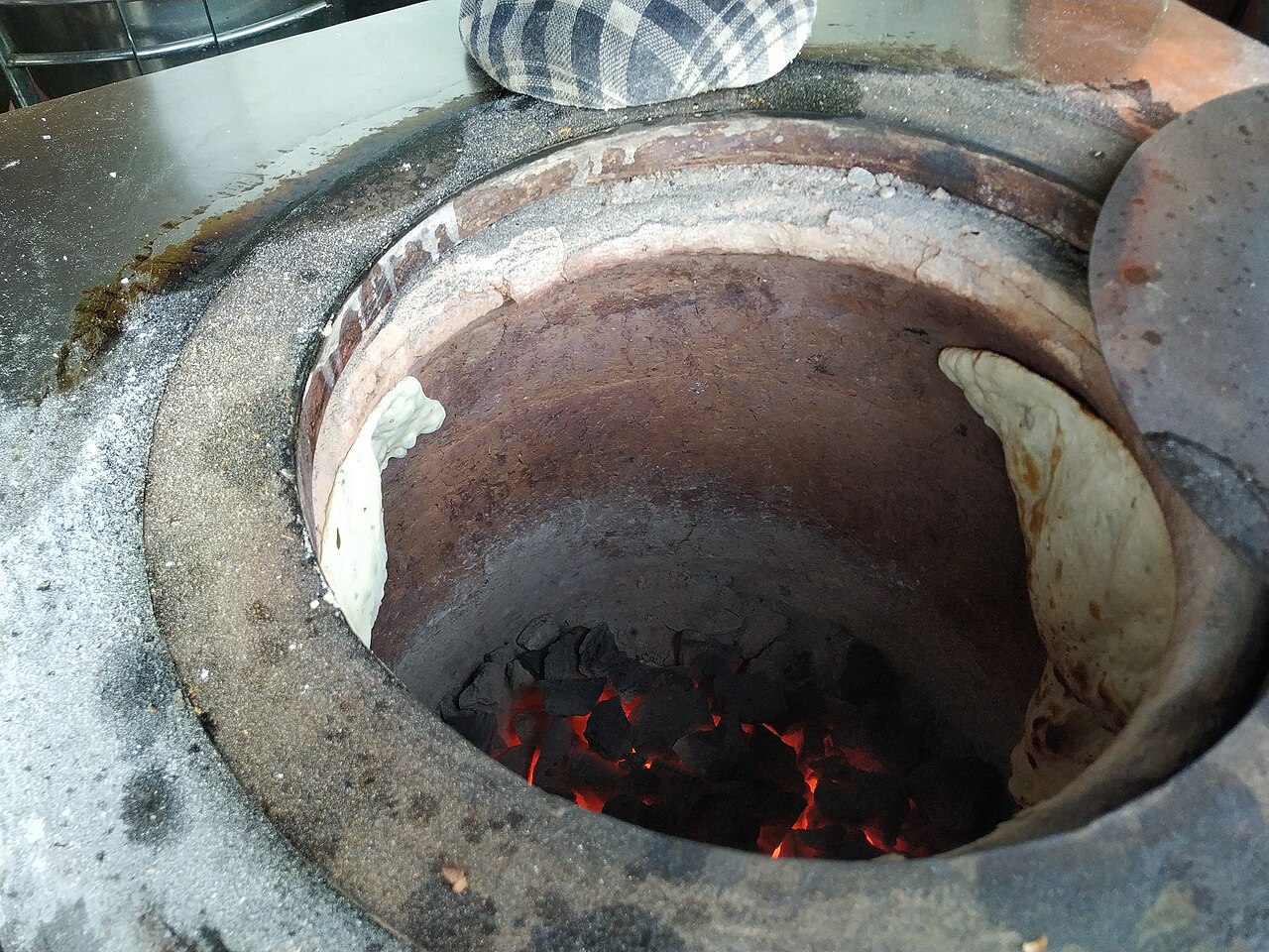 Traditional clay tandoor oven with naan bread cooking inside